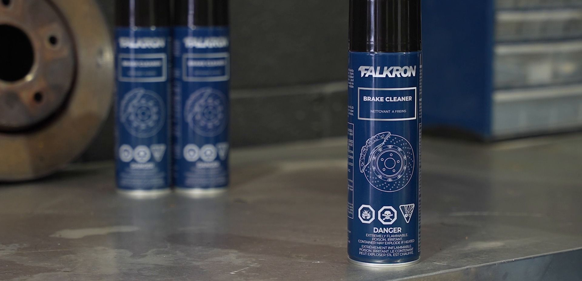 Three cans of FALKRON Brake Cleaner on a steel workbench beside a brake rotor