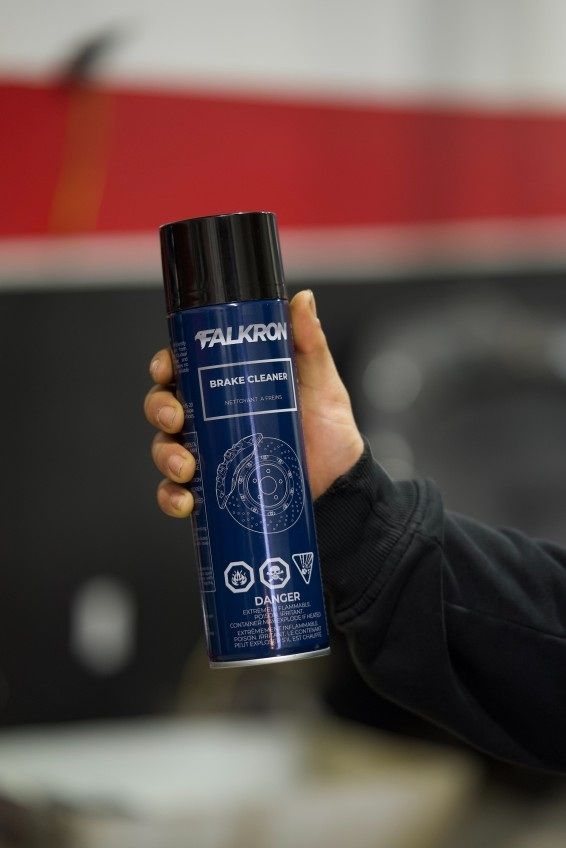 A hand holding a can of FALKRON Brake Cleaner in a workshop