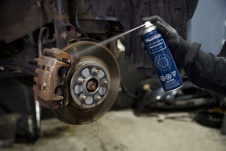 A gloved hand spraying FALKRON Brake Cleaner onto a brake disc and caliper
